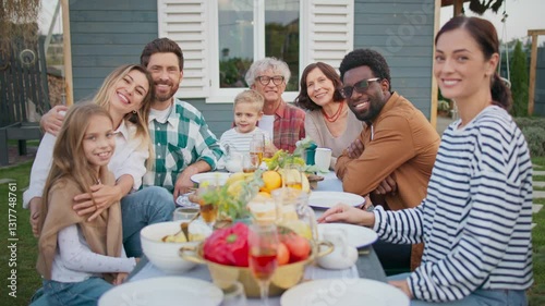 Wallpaper Mural Cute family sitting together at table in front of cozy house. Having dinner in fresh air. Looking at camera while smiling. People having fun together. Tasty dishes on table. Evening in village. Torontodigital.ca