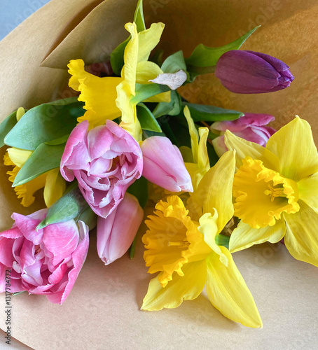 Beautiful composition of the first spring flowers with leaves in a bouquet. Yellow daffodils, pink tulips in a bouquet on craft paper