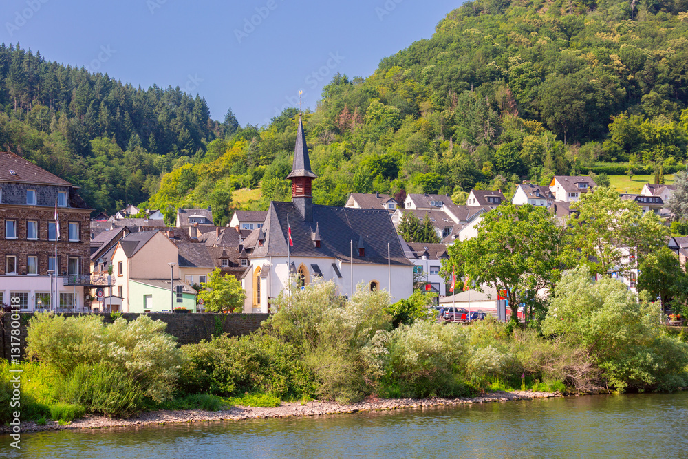 Traditional village with a church, houses, and greenery on the Moselle River near Cochem, Germany, on a sunny day