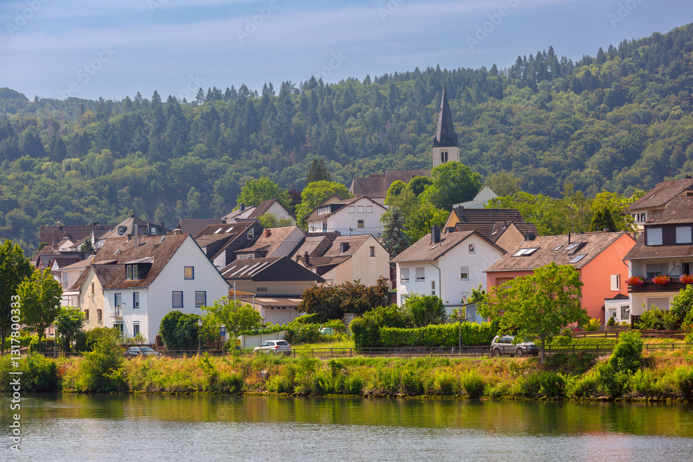 Traditional village with a church, houses, and greenery on the Moselle River near Cochem, Germany, on a sunny day