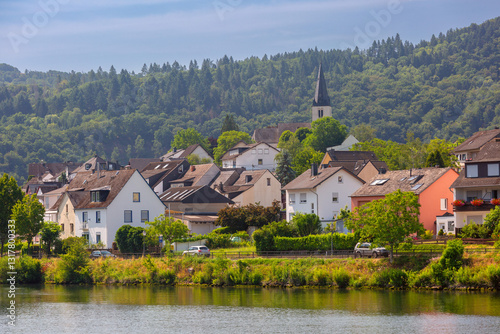 Obraz na płótnie Traditional village with a church, houses, and greenery on the Moselle River near Cochem, Germany, on a sunny day w salonie