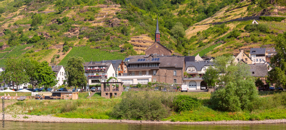Traditional village with a church, houses, and greenery on the Moselle River near Cochem, Germany, on a sunny day