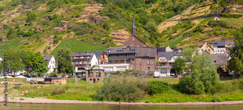Obraz na płótnie Traditional village with a church, houses, and greenery on the Moselle River near Cochem, Germany, on a sunny day w salonie