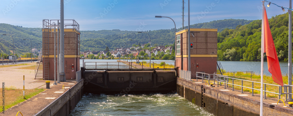 Navigation lock on the Moselle River with water flow, control towers, and a village in the background in Germany