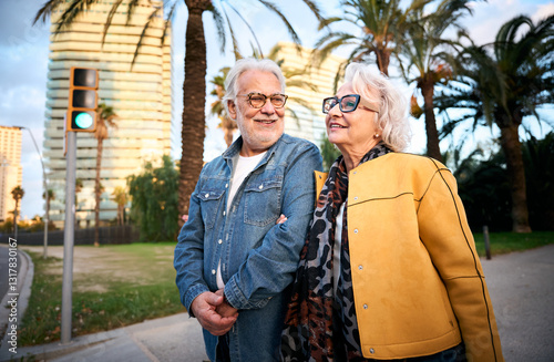 An elderly couple stands together at a crosswalk, waiting for the traffic light to change. Their quiet connection highlights care and companionship amidst the urban surroundings