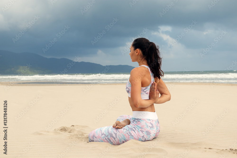 Woman Meditating on Beach During Stormy Weather Practicing Yoga in White Top and Colorful Pants with Dramatic Sky Woman Meditating on Beach During Stormy Weather Practicing Yoga in White Top and Colorful Pants with Dramatic Sky