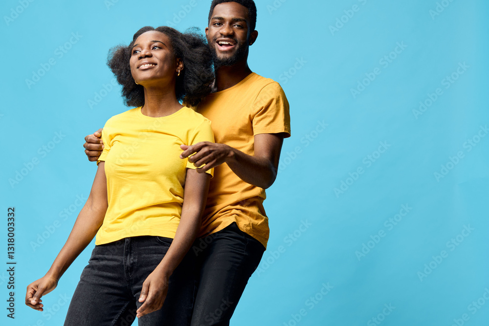 Obraz premium Happy couple in matching yellow t shirts, expressing joy and playfulness against a vibrant blue background, ideal for youth and relationship concepts