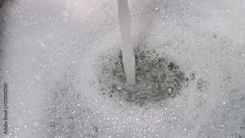 Macro view of kitchen faucet filling sink with soapy water.  Close up view of household chores, water and soap bubbles.