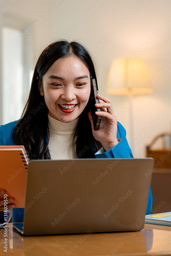 Smiling businesswoman working from home, talking on mobile phone and using laptop, holding notebook