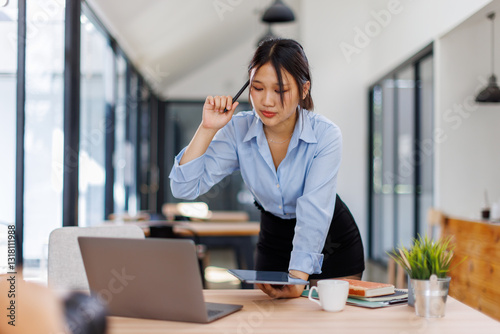 Female asian business person using digital tablet and laptop or remote working at office, looking at digital tablet watching webinar, learning training, studying online seminar or video calling.
