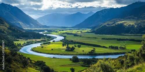 A river flows through a valley with mountains in the background. The scene is peaceful and serene, with the water reflecting the sky and the mountains in the distance