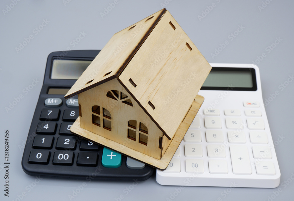 Two calculators and wooden house model on gray background. Costs of house concept. Two calculators and wooden house model on gray background. Costs of house concept.