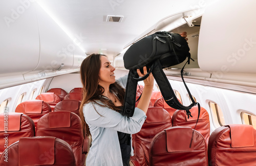 A woman is pulling out a backpack from a red seat on an airplane. Concept of travel and adventure, as the woman is preparing for a journey