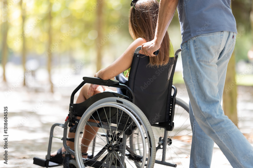 Obraz premium Man pushing woman in wheelchair in park during sunny day