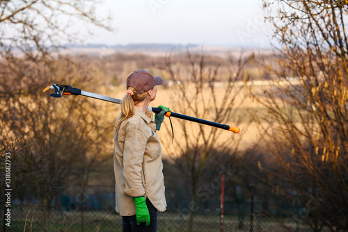 Female farmer holding long pruning shears and preparing for tree maintenance work in orchard