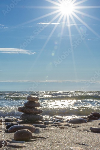 Pebble tower on sunny beach sea wave splashing water balance pyramid harmony equilibrium peace of mind. Cobblestone formation construction seaside