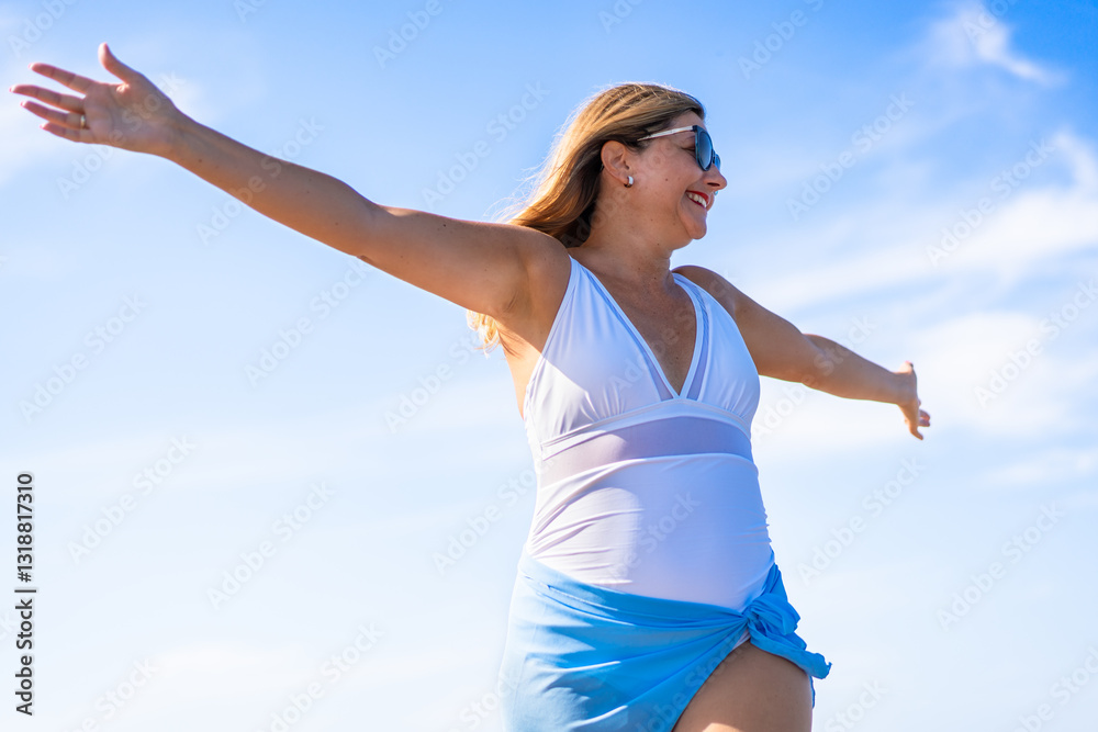 Portrait of beautiful happy middle-aged woman in swimsuit standing against background of blue sky in summertime Portrait of beautiful happy middle-aged woman in swimsuit standing against background of blue sky in summertime