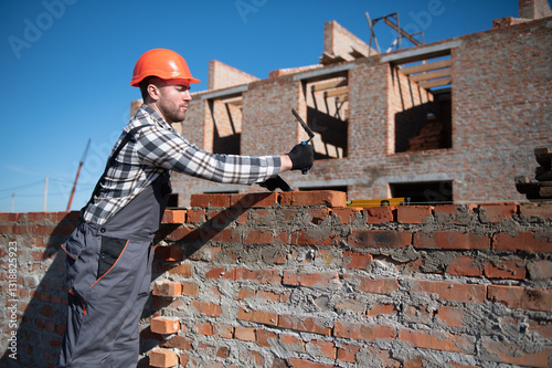 Male construction worker in uniform and helmet on construction of red brick house photo