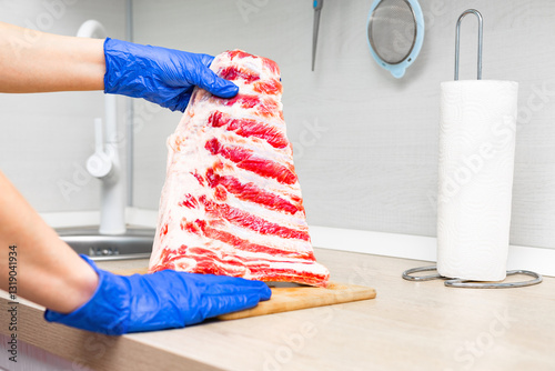 housewife cooking pork ribs in home kitchen. hand holding pork rib. pork rib with layers of fat and red meat. preparing pork ribs for roasting.  photo