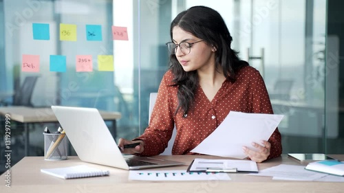 Busy thoughtful young businesswoman analyzing financial documents checking data on laptop sitting at desk at workplace in business office. Financier deals with financial reports, engaged in accounting