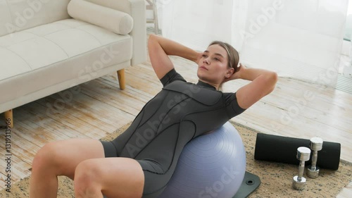 Top view of young caucasian woman doing abdominal exercises while lying on her back on a gym ball in a bright room. The concept of a healthy lifestyle. Sports.