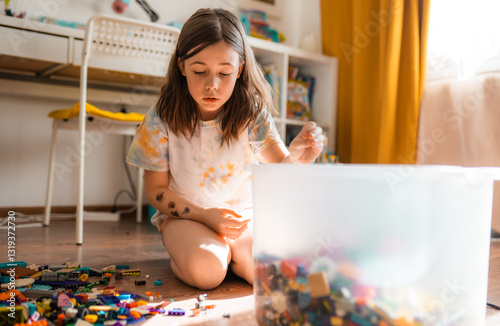 Little girl cleans up her touys in messy room on a floor. Children chores concept.

