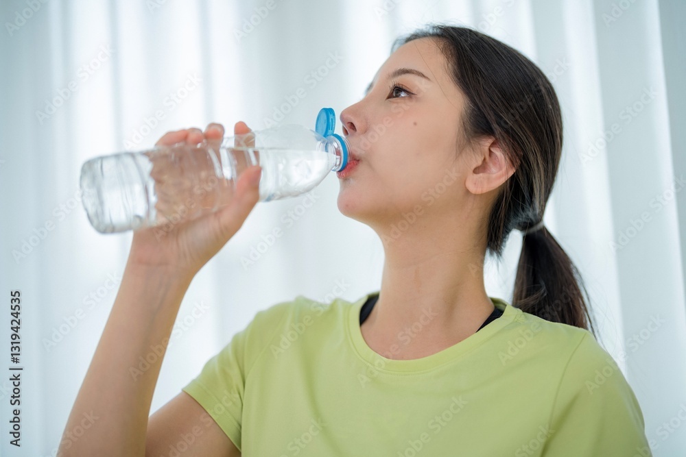 Woman enjoying hydration while relaxing indoors in a light-filled room during daytime Woman enjoying hydration while relaxing indoors in a light-filled room during daytime