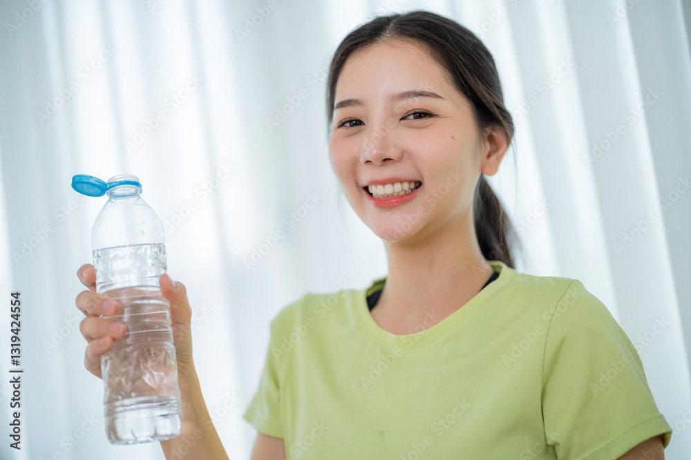 Smiling young woman holding a water bottle in a bright indoor setting during daytime Smiling young woman holding a water bottle in a bright indoor setting during daytime