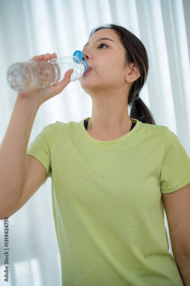 Young woman in green shirt drinks water indoors during workout session for hydration and health Young woman in green shirt drinks water indoors during workout session for hydration and health