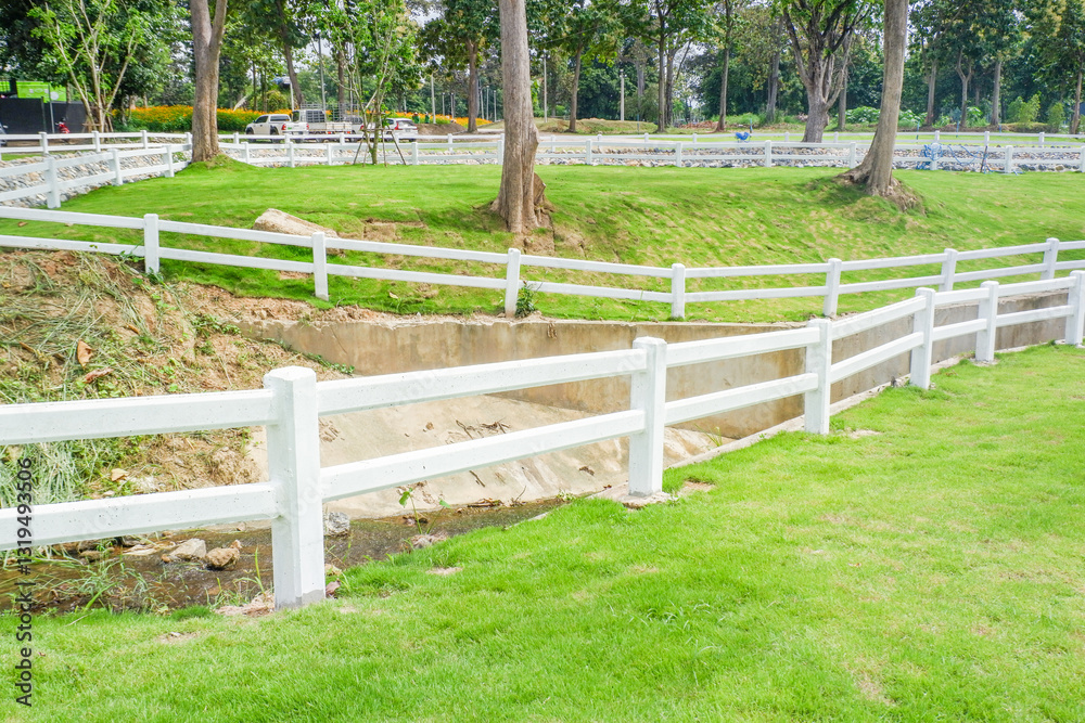 White fence with green grass hill and mountain,blue sky,Lush green golf Course,rest and relax in park near city,big tree in garden,Green grass field,Nature landscape,space for text. White fence with green grass hill and mountain,blue sky,Lush green golf Course,rest and relax in park near city,big tree in garden,Green grass field,Nature landscape,space for text.