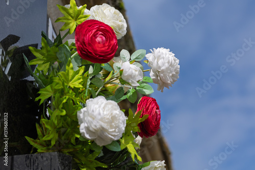 Red and white flowers adorning a tombstone under a blue sky