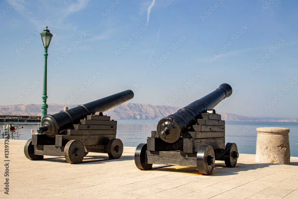 Two old antique military defense cannons in a port pointing at sea. Island in background Two old antique military defense cannons in a port pointing at sea. Island in background