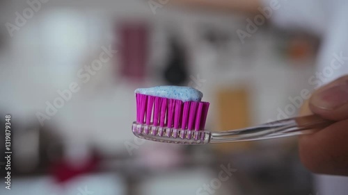 The paste from the tube is squeezed onto the purple bristles of a toothbrush.