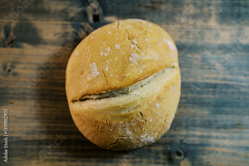 Round loaf of bread with a longitudinal furrow lies on an old shabby wooden table