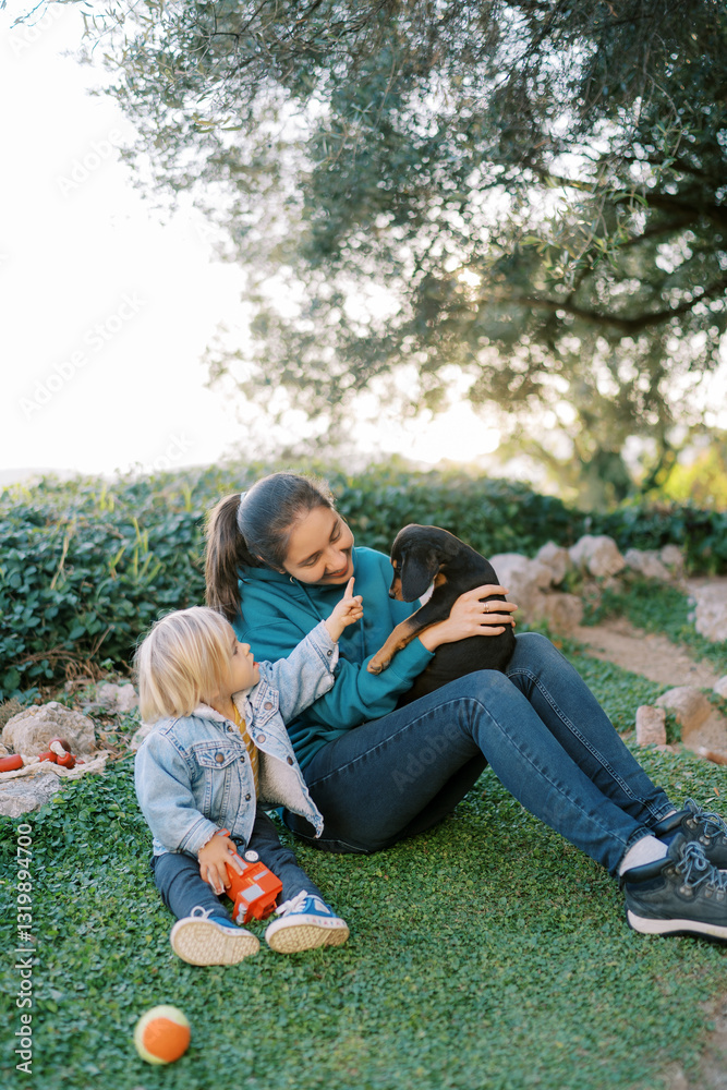 Little girl reaches out with her finger to a big puppy sitting on her mother lap Little girl reaches out with her finger to a big puppy sitting on her mother lap