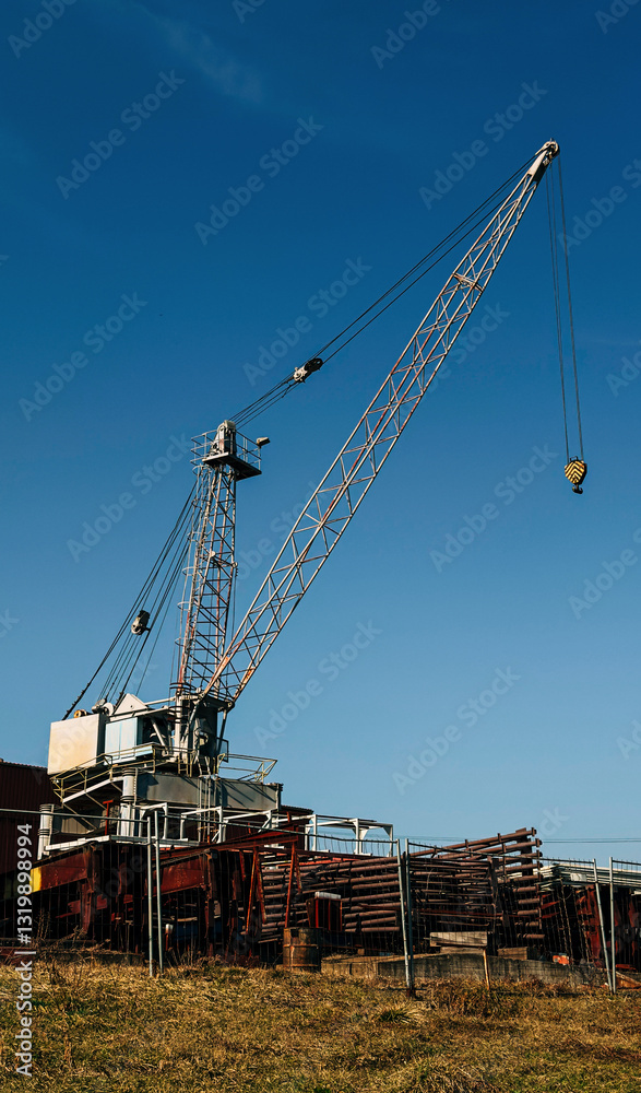 Large industrial crane towering over a construction site with stacked metal beams Large industrial crane towering over a construction site with stacked metal beams