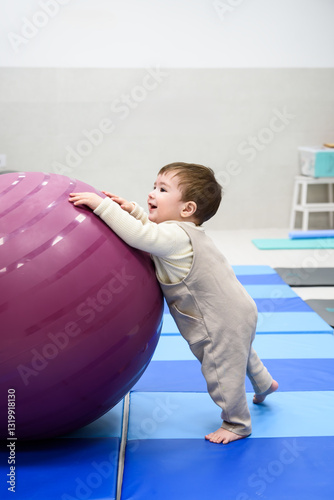 Baby boy playing with purple exercise ball in gym
