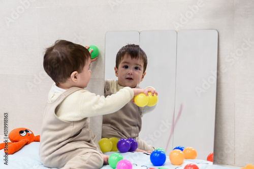 Baby boy playing with colorful balls and discovering himself in the mirror