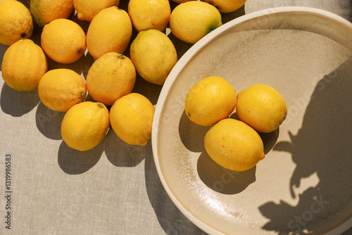 Multiple lemons spread across a surface with three placed in a plate,