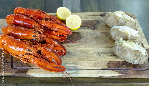 Four whole lobsters from Maine on wood cutting board with a baked potato photo