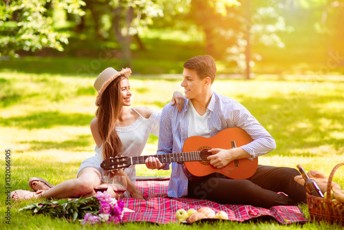 Tableau sur toile Romantic young guy singing song and playing guitar to his beloved woman on picni