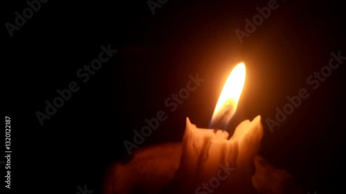 A single candle burns softly in a dark and quiet room, its flickering flame casting moving shadows on the walls. The warm golden glow creates a peaceful and intimate atmosphere, calm and tranquility