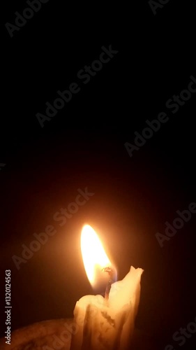 A single candle burns softly in a dark and quiet room, its flickering flame casting moving shadows on the walls. The warm golden glow creates a peaceful and intimate atmosphere, calm and tranquility