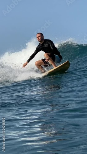 Vertical video of a young man surfing in the clear waters of the Indian Ocean on a sunny day.Bali island.Indonesia