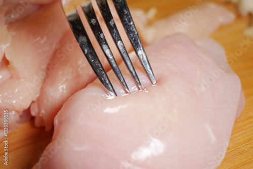Fork piercing raw chicken breast on a wooden cutting board