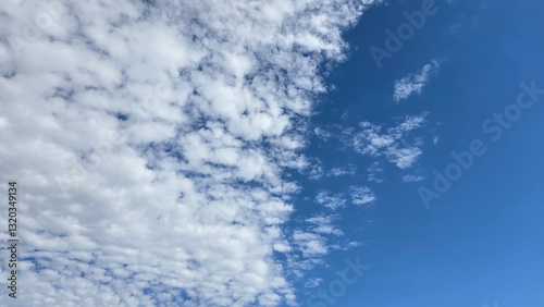 Bright and serene blue sky scattered with fluffy white clouds, depicting the beauty of tranquility. Perfect background for concepts such as freedom, nature, and vastness.