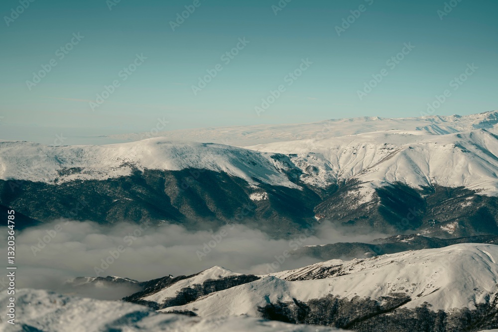 Fototapeta premium Snow-covered mountains under a clear blue sky with clouds in the valley.
