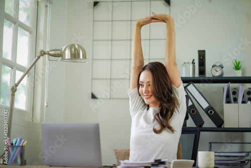 A woman is stretching her arms and legs while sitting at a desk with a laptop