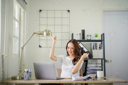 A woman is sitting at a desk with a laptop and a stack of papers