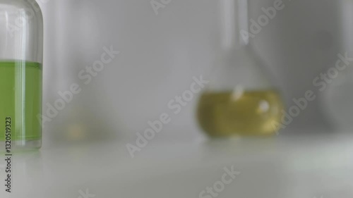 A close-up view of fresh leaves placed in a small cup beside vibrant green liquid and glass containers. The setting suggests a focus on herbal research and formulation techniques.